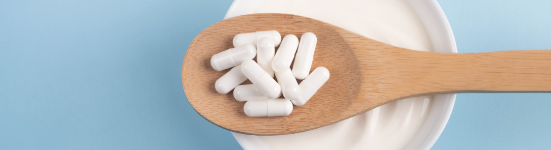 Capsules probiotic on a wooden spoon and bowl with homemade yogurt on light blue background. Fermented foods, dairy, nutritional supplement, healthy digestion concept. Top view, flat lay