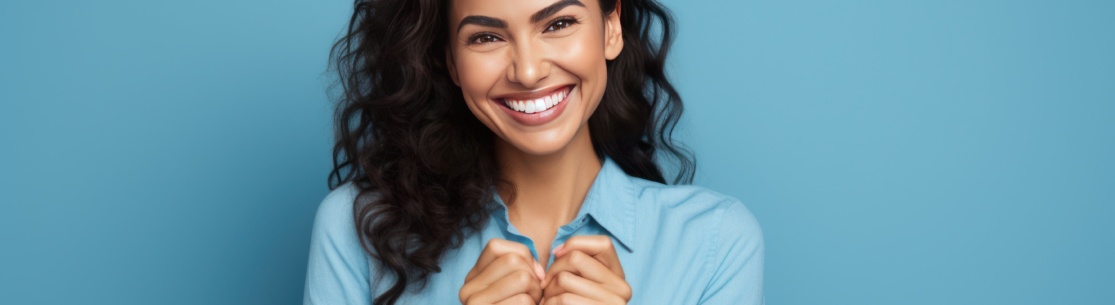 Hispanic woman standing over blue background smiling lovingly and making heart symbol shape with hands. romantic concept. I love you.